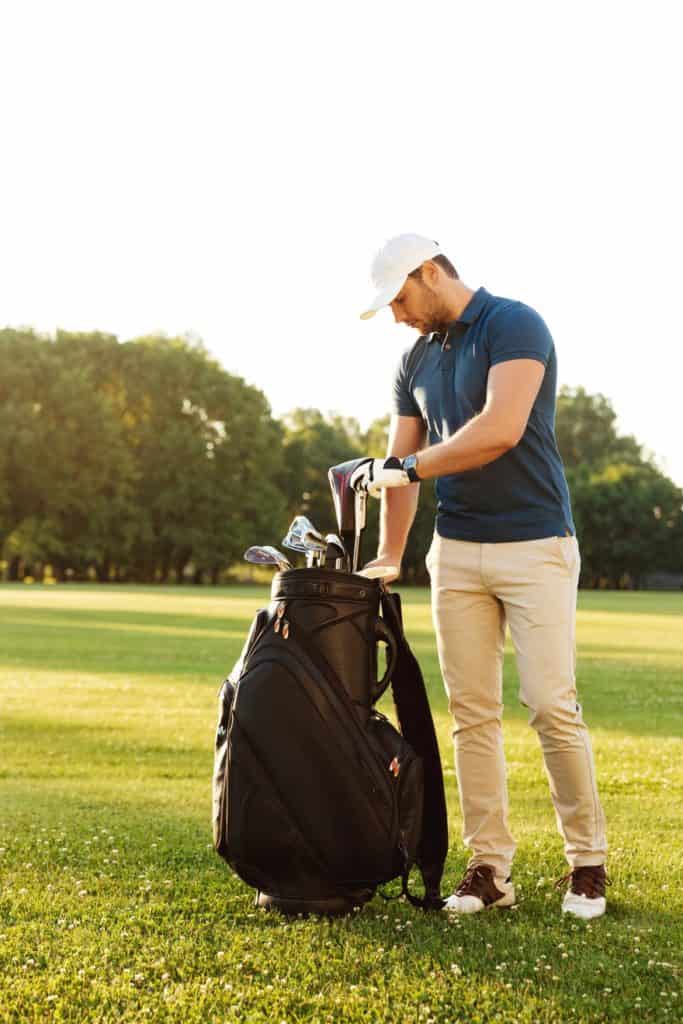 A golfer fixing his golf clubs in a golf bag in the golf course