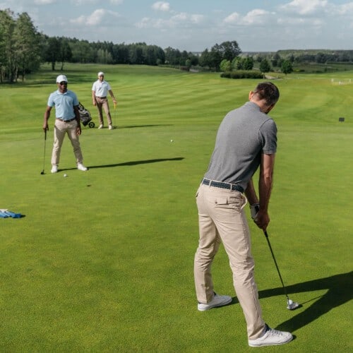 A golfer getting ready for a putting shot on a golf course with two other golfers in the background