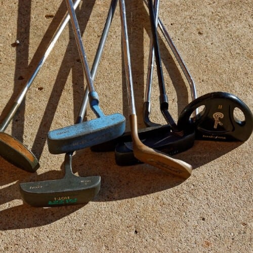 A bunch of used golf clubs on concrete pavement