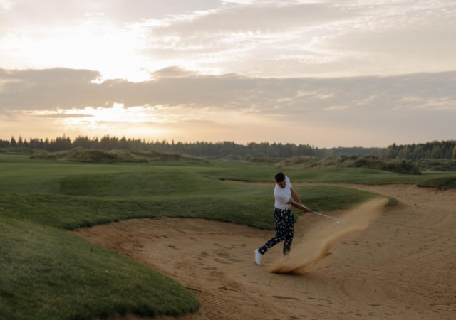A golfer trying to get his golf ball out of the sand pit on a golf course