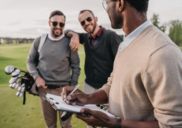 Three golfers on a golf course with on of them holding a clipboard