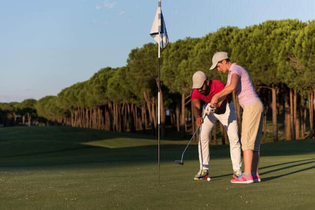 A golf coach teaching a beginner golfer how to properly hold a golf club on the golf course