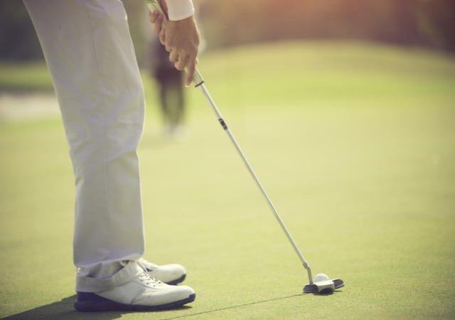 A person with their feet together preparing to put a golf ball on an golf course