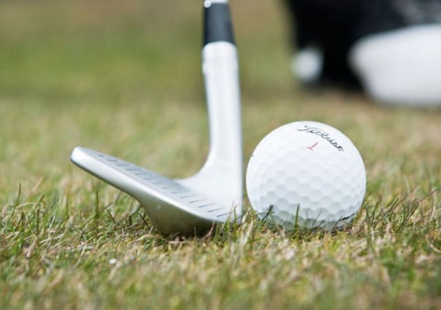 A lofted wedge golf club with a Titleist golf ball on the turf