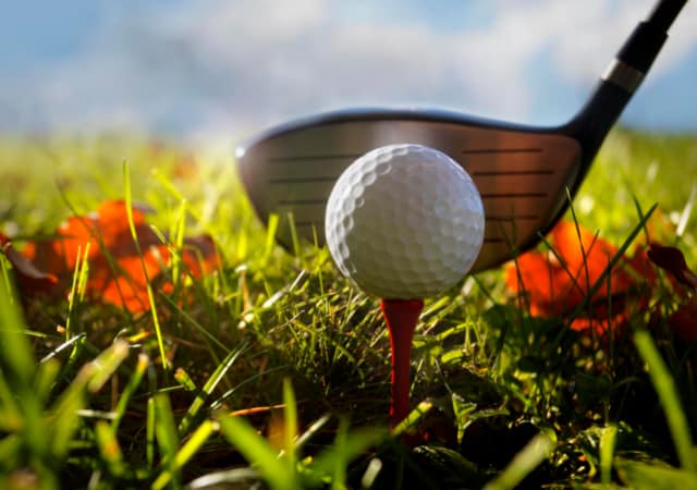 A golf ball on a tee and a golf club on the golf course