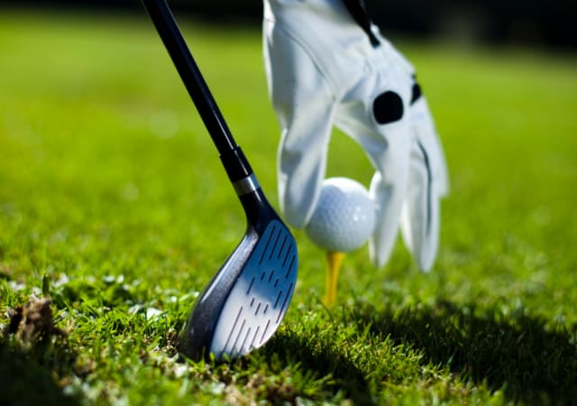 Golfer positioning the golf ball on the tee with a golf club beside it.