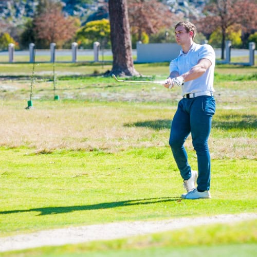 Young male golfer practicing swing on a lush golf course during daytime.